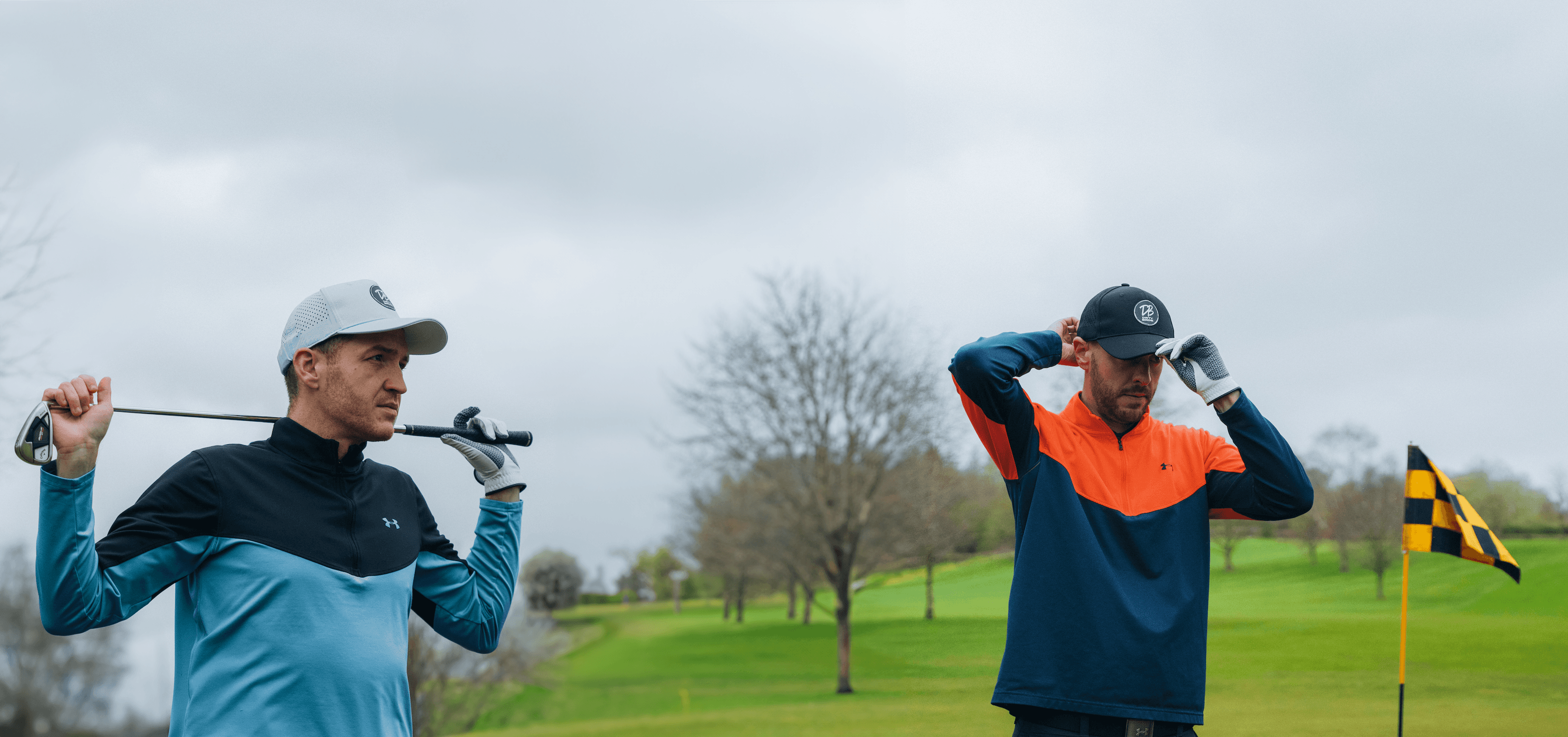 2 golfers Standing on golf course with club behind back and one adjusting golf cap