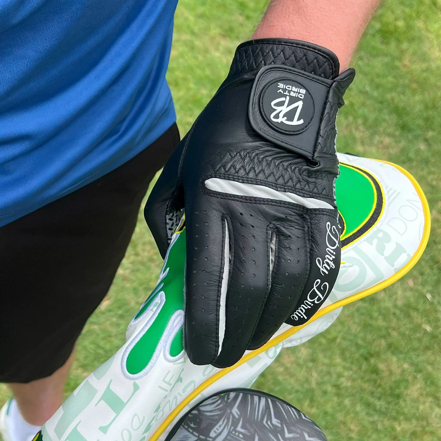 Premium black cabretta leather golf glove holding driver headcover on course showing detailing
