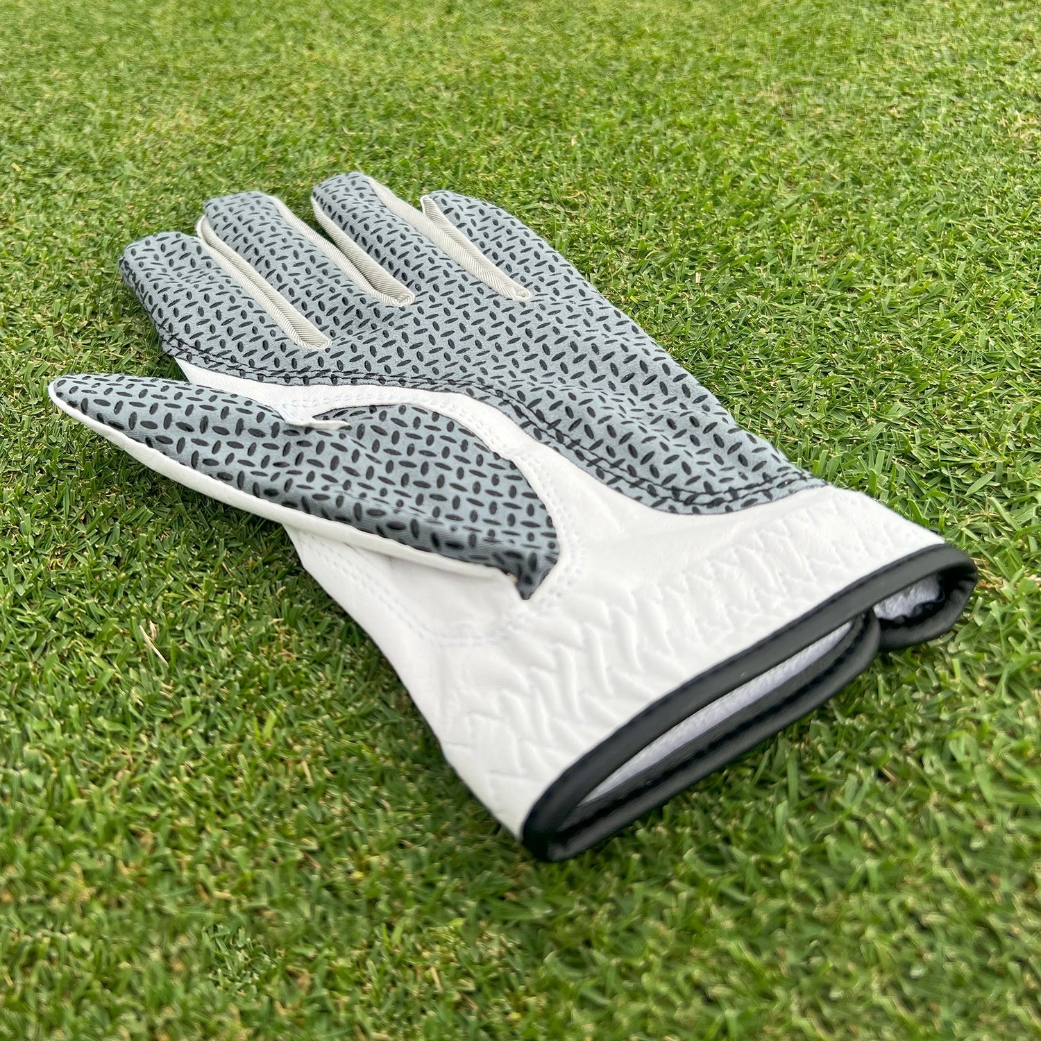 Premium white Cabretta golf glove displayed flat on green, highlighting palm grip texture.