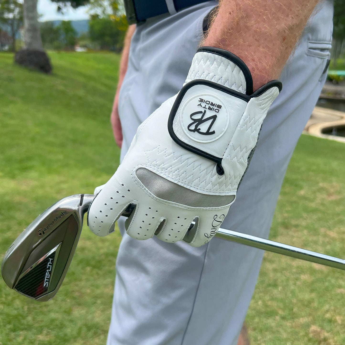 Premium golf glove holding iron shaft on course with logo detailing on show