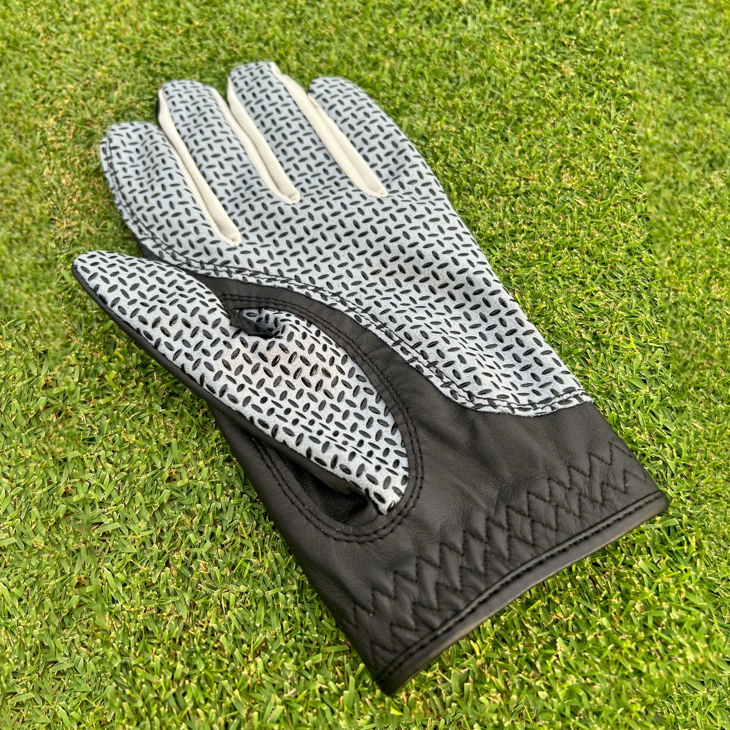 Black golf glove displayed palm-up on green, showcasing grip pattern and premium leather.