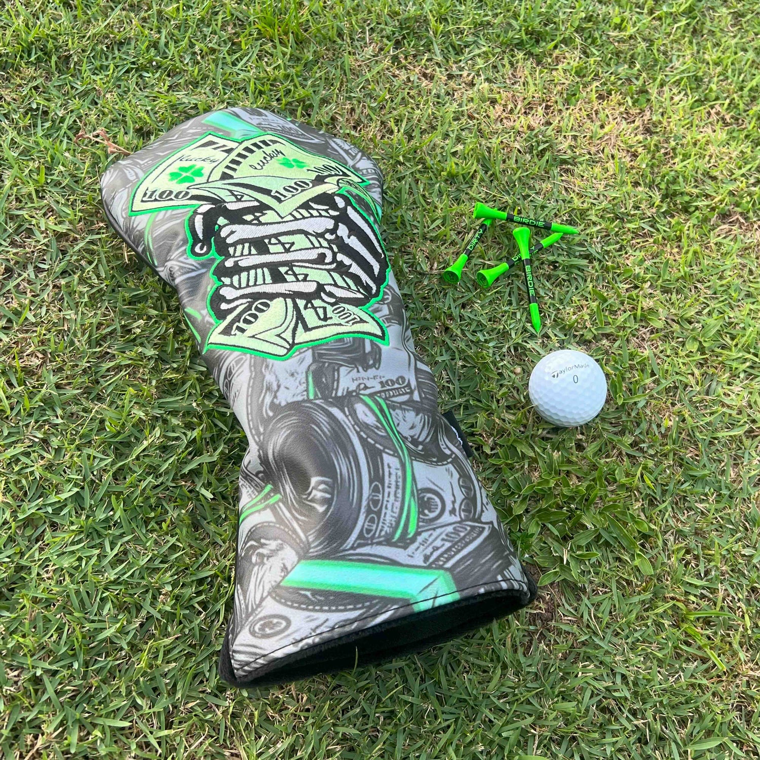 Lucky Money luxury headcover on golf fairway with 3 tees and golf ball.